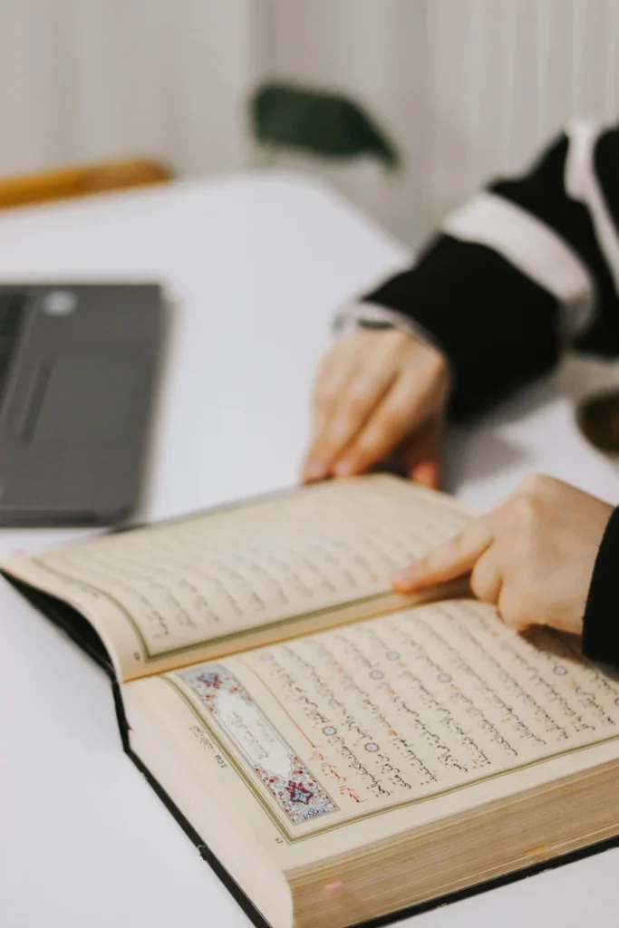 Student’s hands resting on an open Quran beside a laptop on a home desk during a live online Hifz class